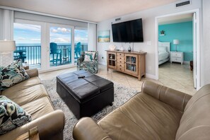 A spacious living room with a large TV, a comfortable sofa set, a wooden cabinet, and a balcony with a view of the sea. - Sea Oats 704 - Coral Shores (Fort Walton Beach)