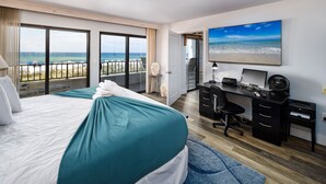 Una habitación de hotel con una cama grande, un escritorio con computadora y vista a la playa.