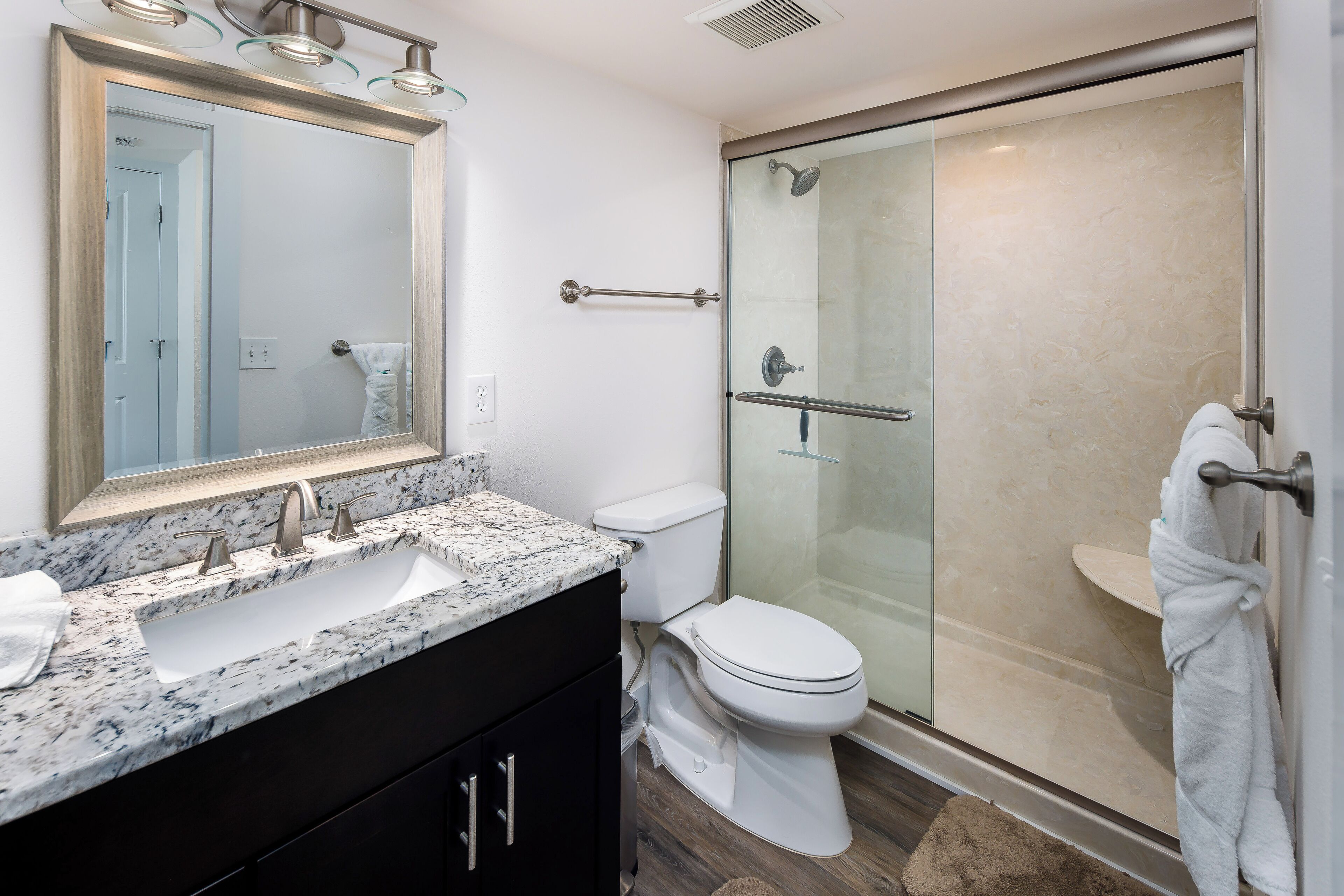 A modern bathroom with a large mirror, two sinks, a toilet, and a glass-enclosed shower.