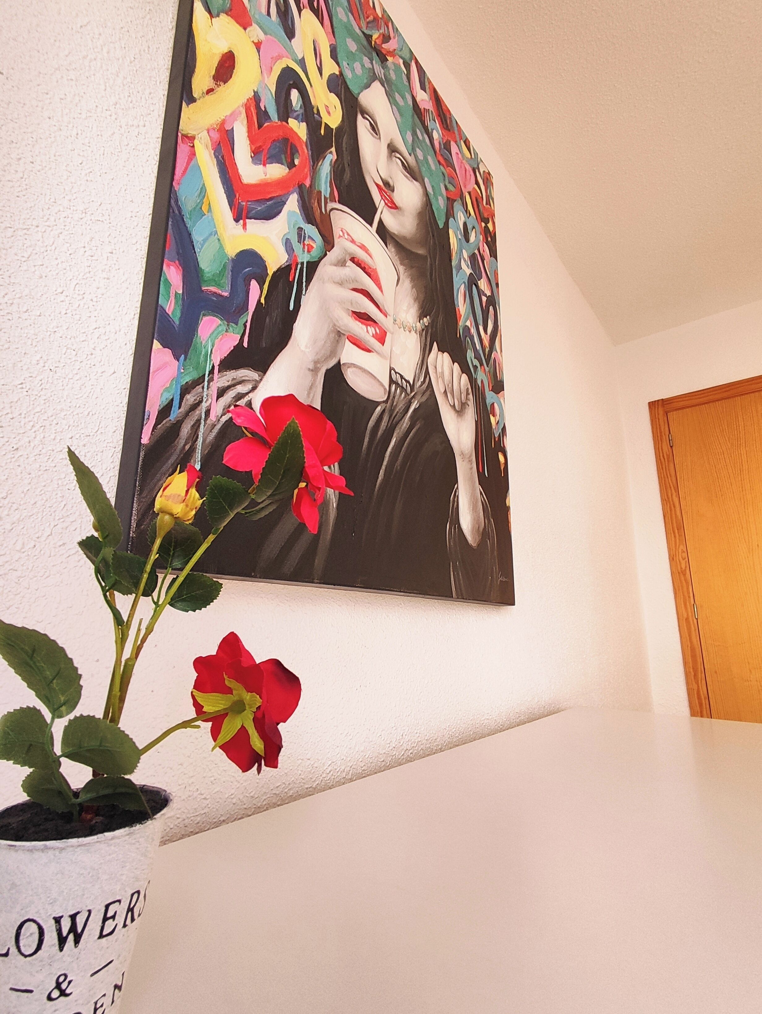 A painting of a woman holding a cup, a potted plant with red flowers, and a wooden door.