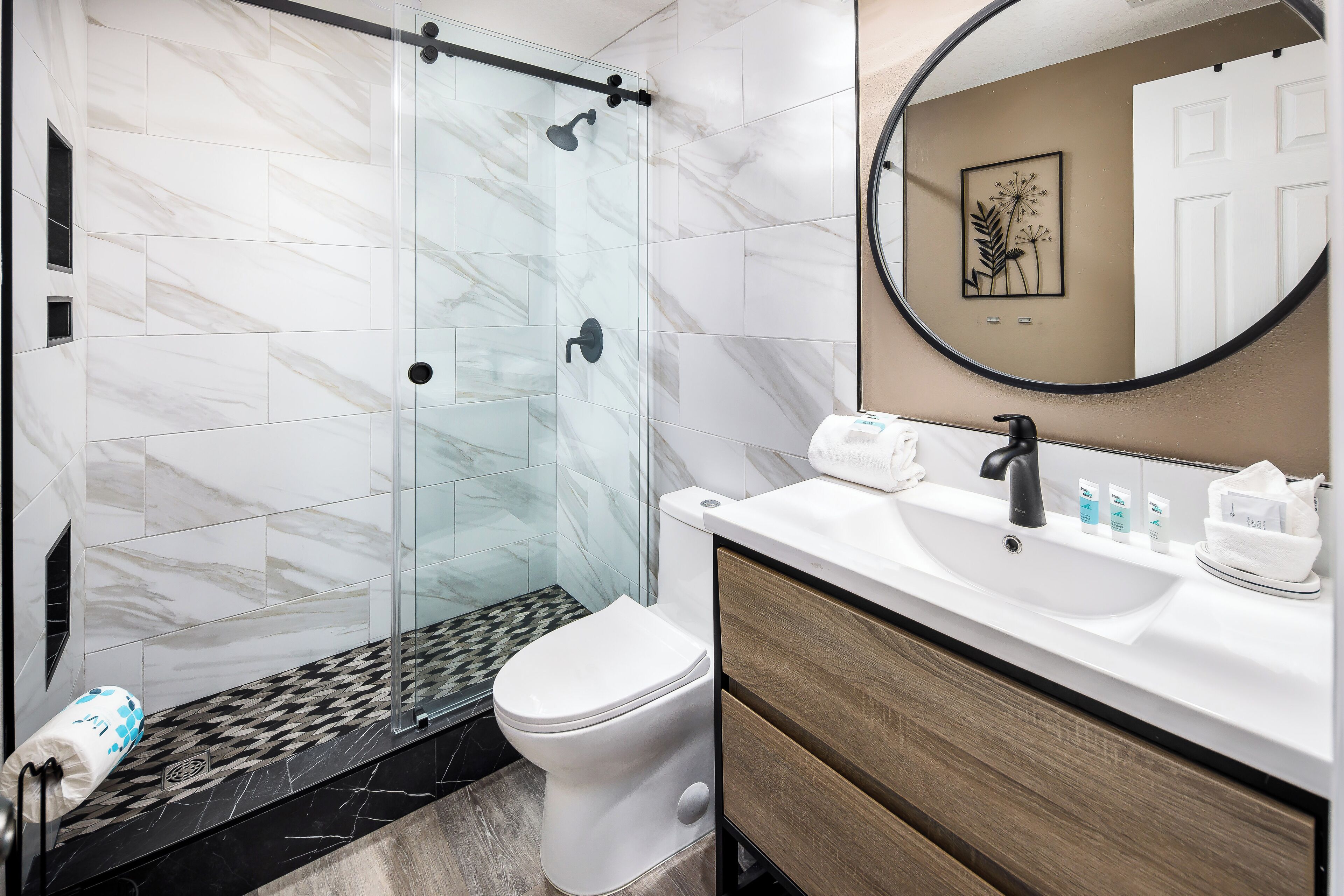 A modern bathroom with a glass-enclosed shower, a white toilet, and a vanity with a sink and mirror.