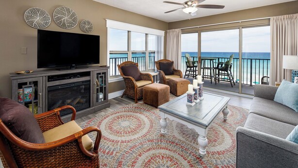 A spacious living room with a flat-screen TV, wicker chairs, a sofa, and a balcony with a view of the ocean. - Emerald Towers West 4000 - Ocean Kissed (Fort Walton Beach)