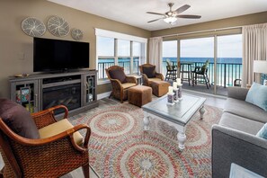 A spacious living room with a flat-screen TV, wicker chairs, a sofa, and a balcony with a view of the ocean. - Emerald Towers West 4000 - Ocean Kissed (Fort Walton Beach)