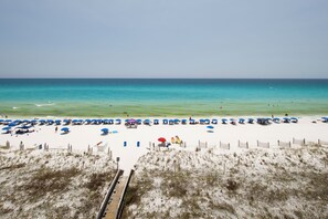 A beach with a wooden boardwalk leading to the shore, sandy beach, and clear blue water. - Surf Dweller 607 - Salt & Sky Haven (Fort Walton Beach)