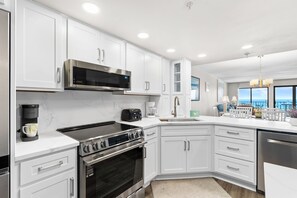 A modern kitchen with white cabinetry, a built-in microwave, a stovetop, and a dishwasher. - Surf Dweller 607 - Salt & Sky Haven (Fort Walton Beach)