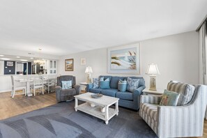 Ein Wohnzimmer mit einem blauen Sofa, einem grauen Sessel, einem weißen Couchtisch und einem Essbereich mit einem weißen Tisch und Stühlen.