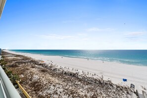 A beach with a clear sky, sandy shore, and a few people walking. - Pelican Isle 613 - Salty Sunsets (Fort Walton Beach)