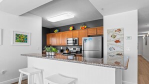 Eine moderne Küche mit Holzschränken, Edelstahlgeräten, einer Granit Arbeitsplatte und weißen Barhocker.