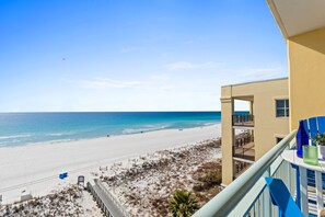 A beach view from a balcony with a clear sky, a sandy beach, and a building with a balcony. - Pelican Isle 613 - Salty Sunsets (Fort Walton Beach)