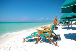 A beach with rows of wooden beach chairs and a green umbrella. - Gulf Dunes 510 - The Wave Crest (Fort Walton Beach)