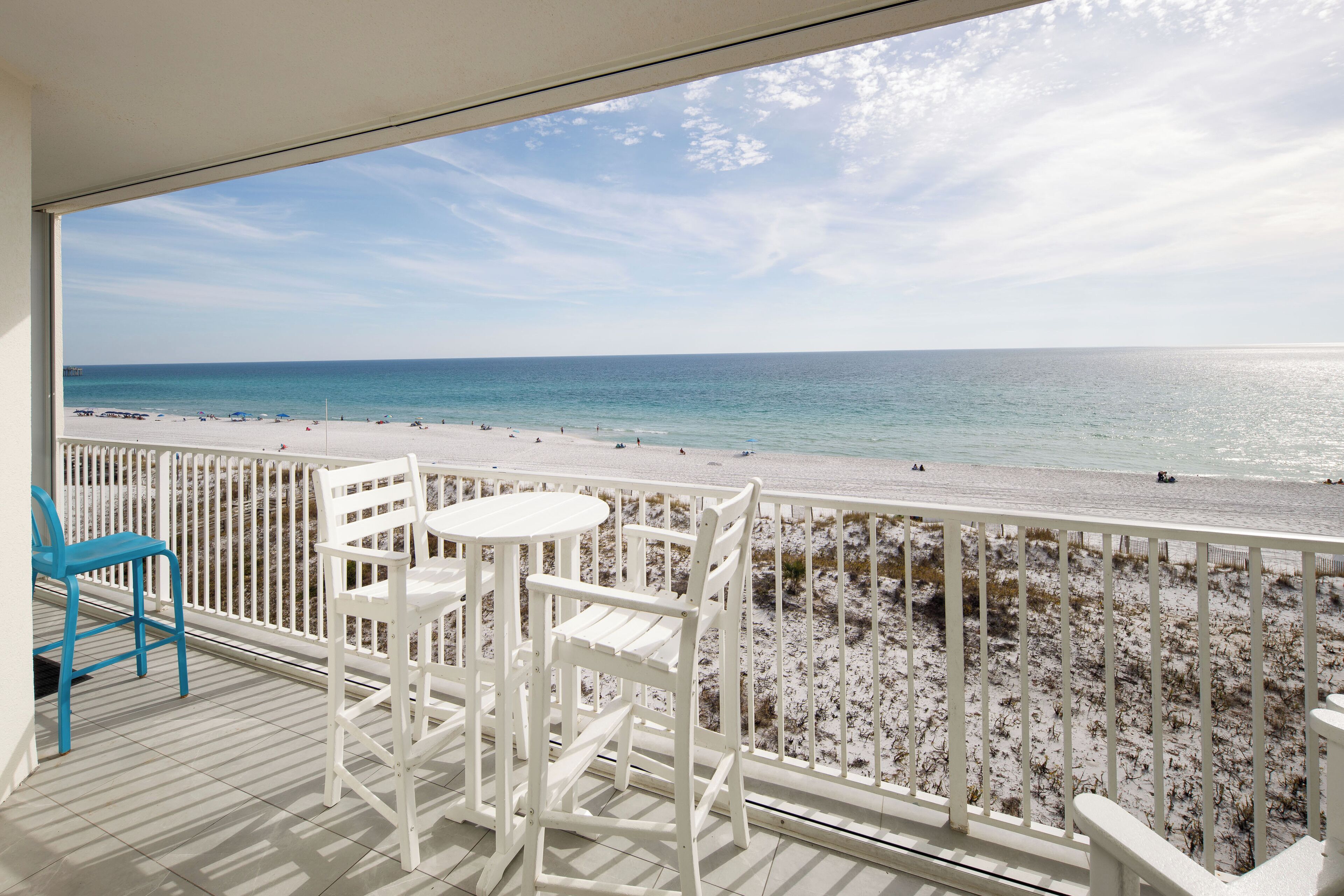 Een balkon met witte stoelen en een tafel, met uitzicht op een strand met een zandstrand en de oceaan.