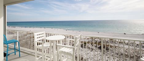 Un balcón con sillas y una mesa blancos, con vista a una playa de arena y al océano.