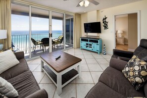 A living room with a sofa, a coffee table, a TV, and a balcony with a view of the ocean. - Island Princess 701 - Beach Bum Bliss (Fort Walton Beach)
