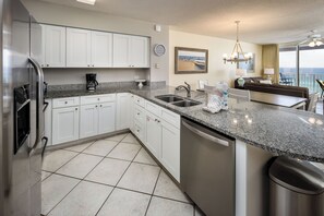 A modern kitchen with white cabinets, a granite countertop, stainless steel appliances, and a view of the ocean through a balcony. - Island Princess 701 - Beach Bum Bliss (Fort Walton Beach)