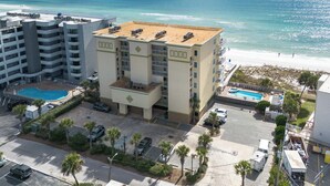 Un hotel con piscina en la azotea, vistas a la playa y un estacionamiento con varios coches.