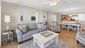A living room with a grey sofa, a white coffee table, and a dining area with a white table and chairs. - Gulf Dunes 410 - Shimmering Sea (Fort Walton Beach)