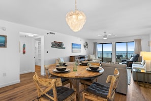 Sala moderna com mesa de jantar de madeira, assentos confortáveis, ventilador de teto e janelas amplas com vista.