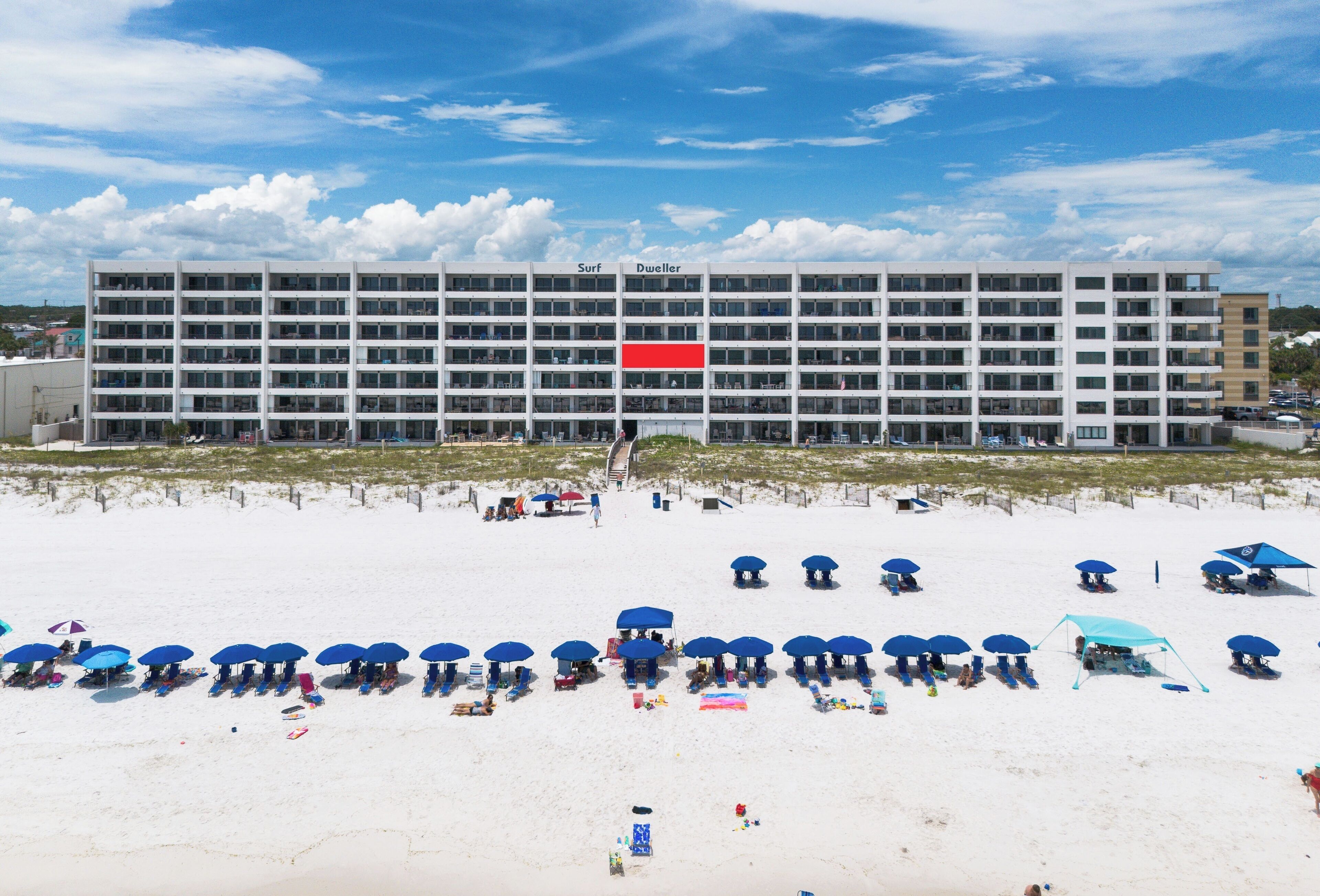 Ein Hotel mit mehreren Stockwerken und einer Strandanlage mit Sonnenschirmen und Liegestühlen.