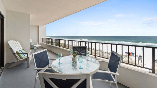 Een balkon met een tafel, stoelen en uitzicht op het strand.