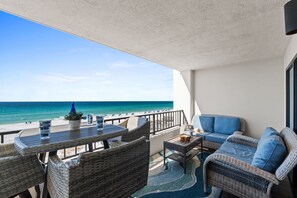 Uma varanda com móveis de vime, uma mesa e vista para a praia e o oceano.