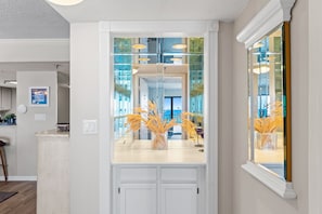 A kitchen with a white countertop, a vase with dried plants, and a glass door leading to a balcony. - Surf Dweller 410 - Seaside Summit (Fort Walton Beach)