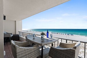 Uma varanda com mobiliário de vime, uma mesa e vista para a praia.