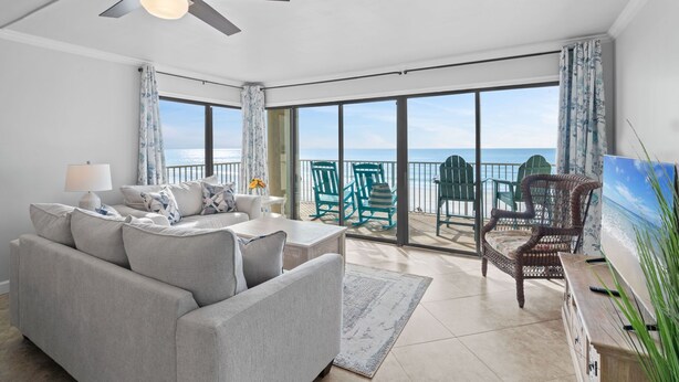 A spacious living room with a large sofa, a ceiling fan, and a view of the ocean through large windows. - Gulfside 401 - Sunny Side Up (Fort Walton Beach)