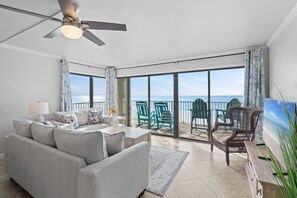 Ein geräumiges Wohnzimmer mit einer großen Couch, einem Deckenventilator und Meerblick durch große Fenster.