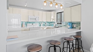 A modern kitchen with white cabinets, a large island with stools, a microwave, and a coffee maker. - Gulfside 401 - Sunny Side Up (Fort Walton Beach)