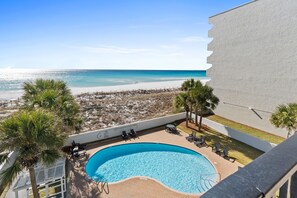 Ein Pool mit Blick auf den Strand, umgeben von Palmen und Liegestühlen.