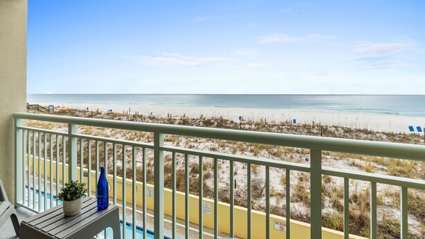 A balcony with a view of the beach, a pool, and a blue bottle on the table. - Pelican Isle 216 - Surfside Haven (Fort Walton Beach)