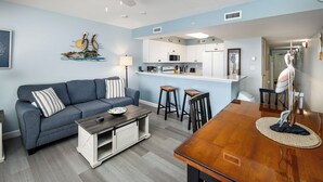 A modern living room with a sofa, coffee table, and kitchen area. - Pelican Isle 307 - Sunkissed & Vibing (Fort Walton Beach)