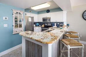 Una cocina con encimera de mármol, armarios blancos y microondas integrado.