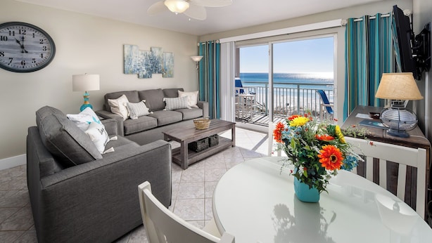 A modern living room with a grey sofa, a round glass table, and a balcony with a view of the sea.