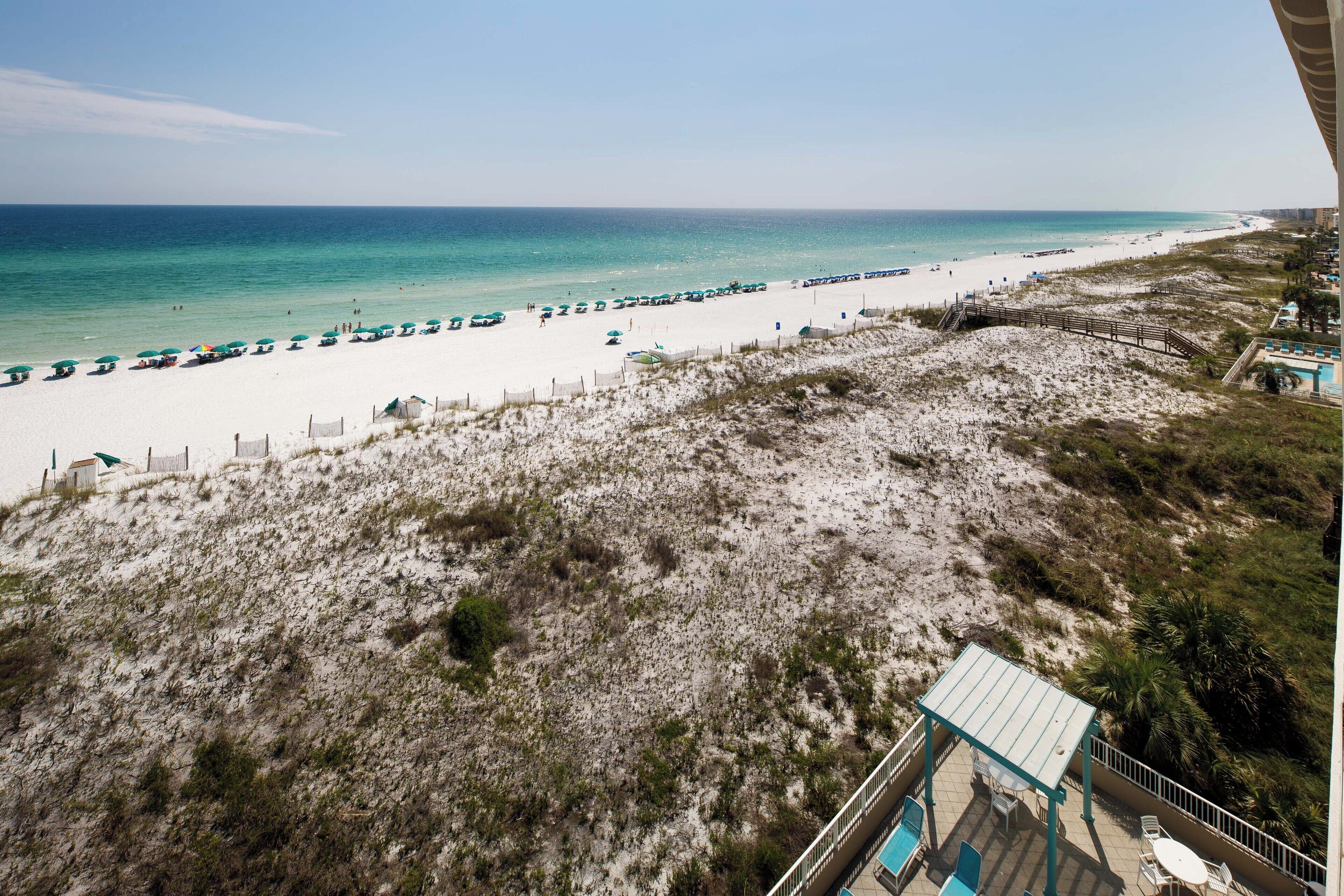 Blick auf einen Strand mit weißem, sandigem Ufer, blauem Himmel und einigen Sonnenschirmen.