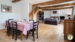 Ein Essbereich mit Tisch für vier Personen, eine Treppe, die zu einem Schlafboden führt, und ein Wohnbereich mit Sofa und Fernseher.