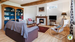 Ein gemütliches Wohnzimmer mit Kamin, Fernseher, Bücherregal und einer bequemen Sitzecke.