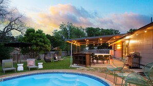 Un patio trasero con piscina, mobiliario exterior y zona de barbacoa.