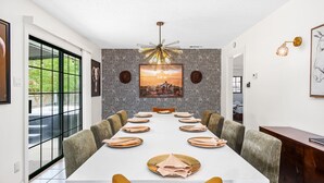 Comedor con una larga mesa dispuesta para 12 personas, rodeada de sillas tapizadas.