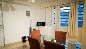 A small, modern room with a glass dining table, two brown chairs, a microwave, a washing machine, and a small plant on the table. - Cozy 3BR + Parking, Near Airport — Solar Backup! (Carolina)