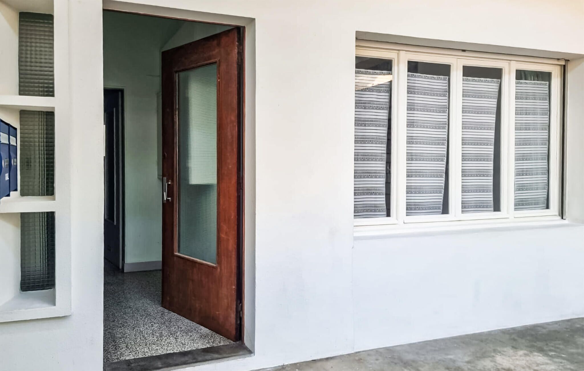 A hallway with a wooden door, a window with striped curtains, and a white wall.
