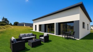 Una casa moderna con techo plano, grandes puertas correderas de vidrio y un patio con mobiliario exterior.