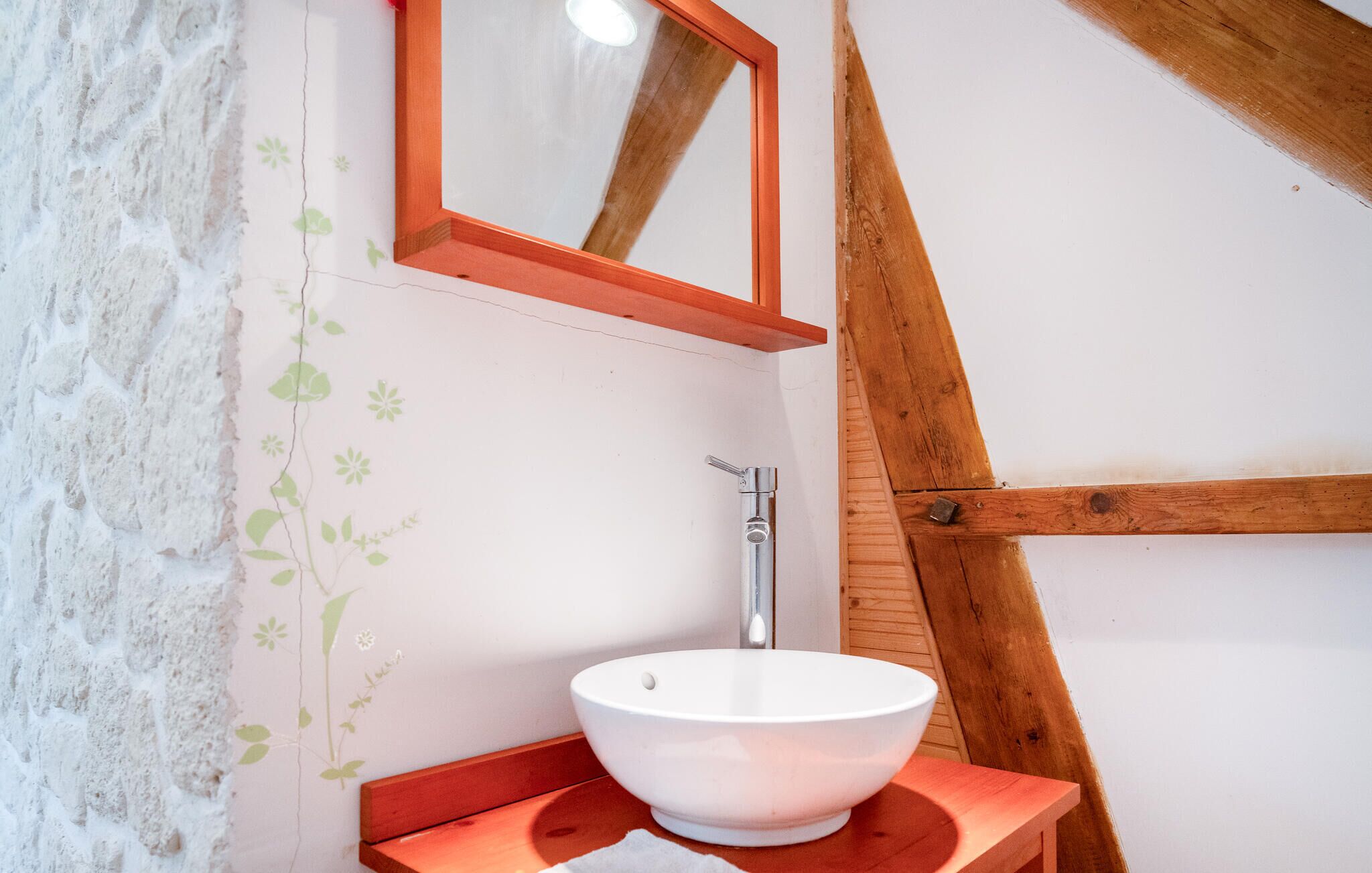 A bathroom with a white basin on a wooden countertop, a wooden beam structure, and a wall with floral wallpaper.