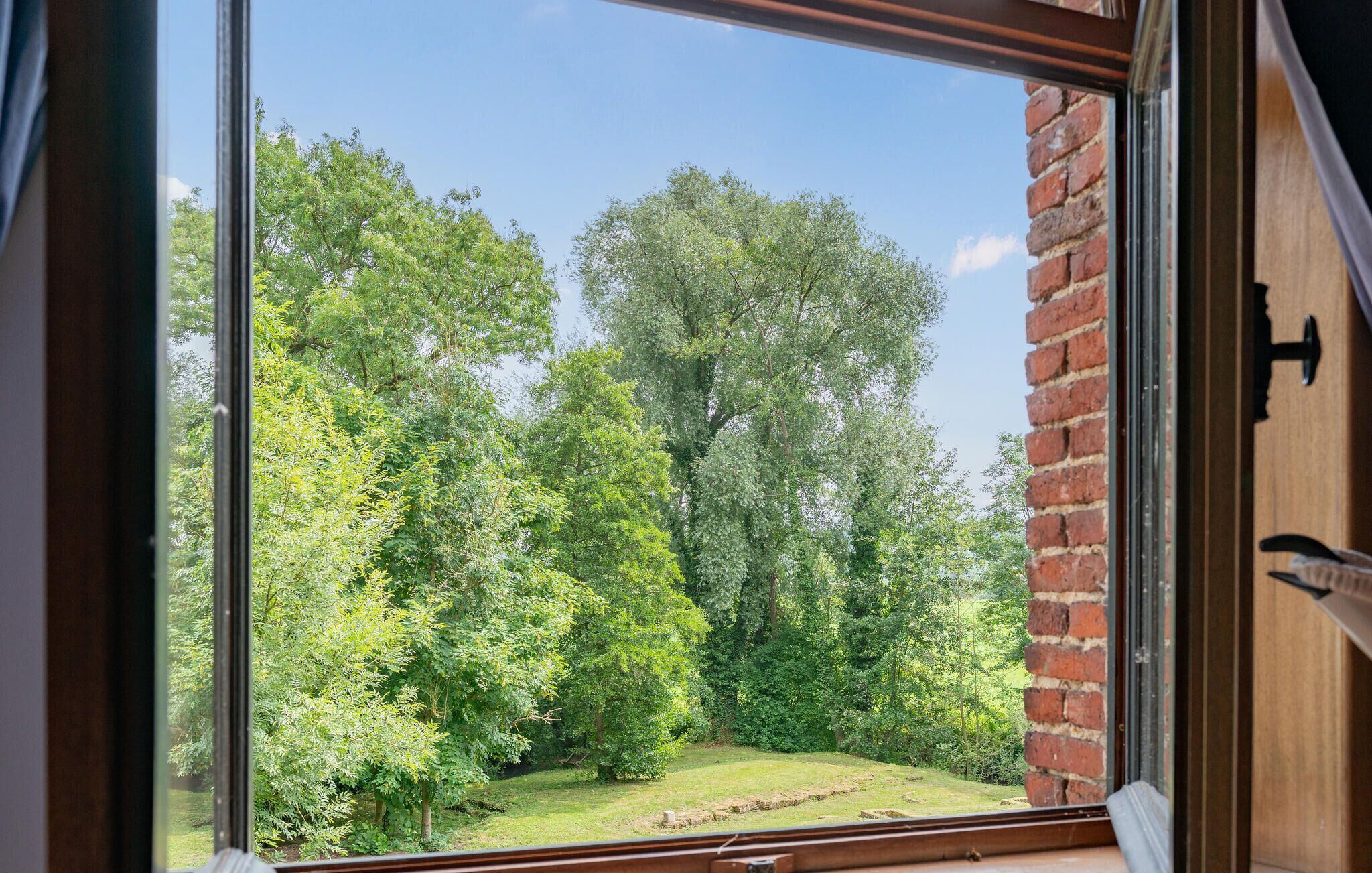 Vista a través de una ventana que muestra un muro de ladrillo y un paisaje verde exuberante con árboles.
