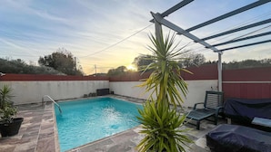 Une piscine rectangulaire avec une terrasse carrelée, entourée d’un petit muret et d’une structure en forme de pergola.