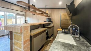Une cuisine moderne dotée d’un îlot en pierre, d’étagères en bois, d’un four encastré et d’un grand évier.