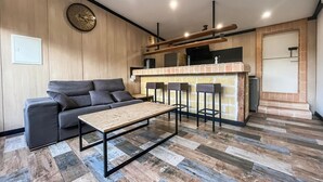 Un salon moderne comprenant un canapé, une table basse et un coin cuisine avec un mur arrière en briques et des tabourets de bar.