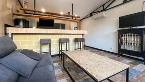 Un salon moderne avec un canapé gris, une table basse en bois et un coin cuisine doté d’un mur de fond en briques et d’un téléviseur à écran plat.