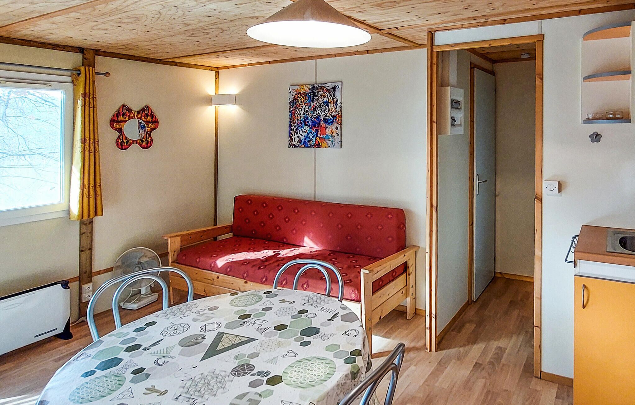 A cozy room with a red sofa, a table with a geometric tablecloth, a wall with a colorful abstract painting, and a wooden ceiling.