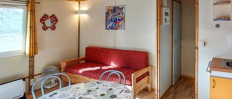 A cozy room with a red sofa, a table with a geometric tablecloth, a wall with a colorful abstract painting, and a wooden ceiling.